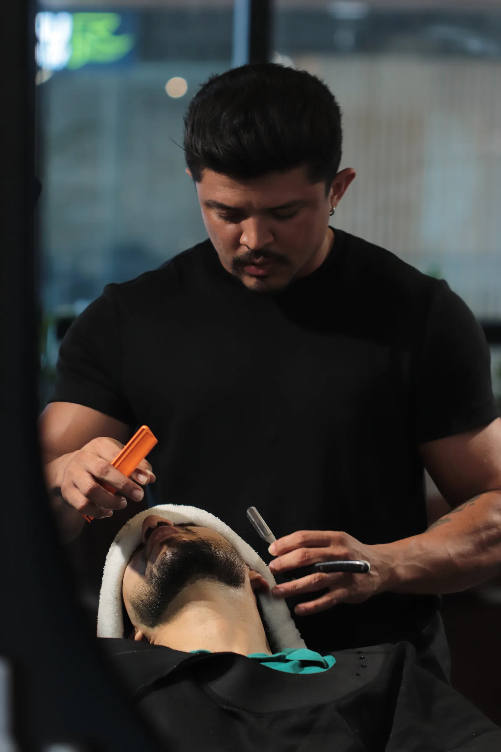 Barbeiro modelando a barba de um cliente com navalha na MYL Barber Clinic