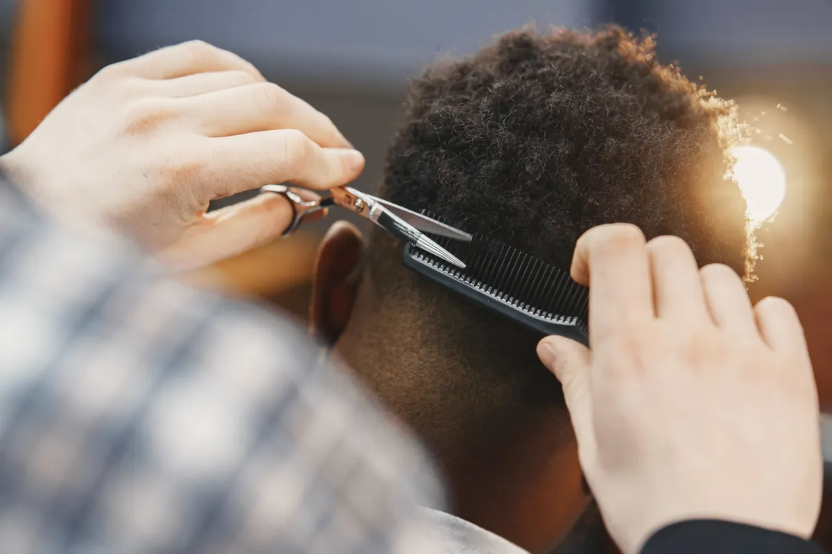 Barbeiro aparando cabelo crespo com tesoura e pente